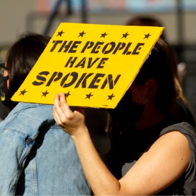 Person holding yellow sign that says The People Have Spoken
